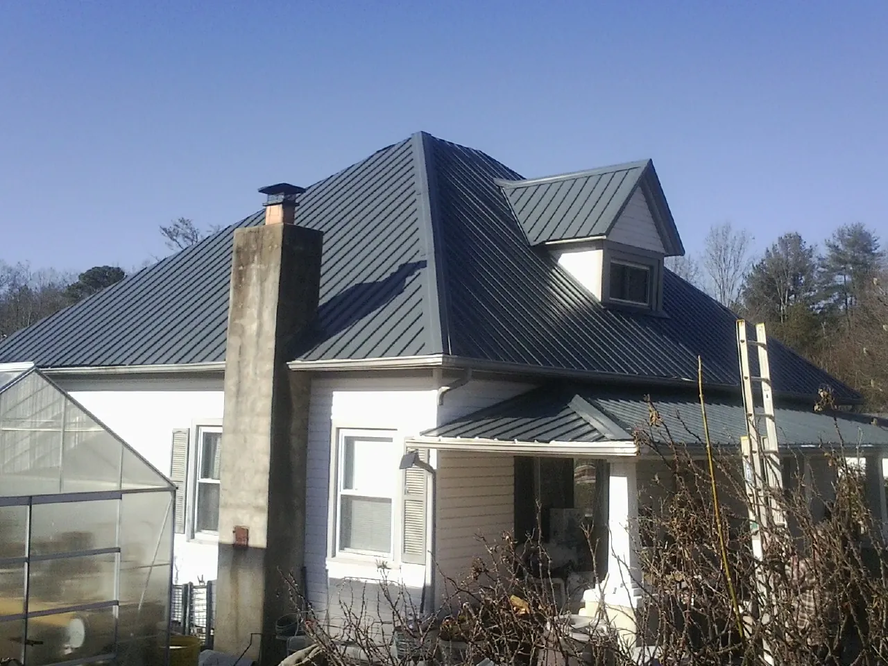 Dark blue standing seam metal roof on a white farmhouse with dormer — Slate & Tile Roof Repair by Roofing Brothers in Newtown Square