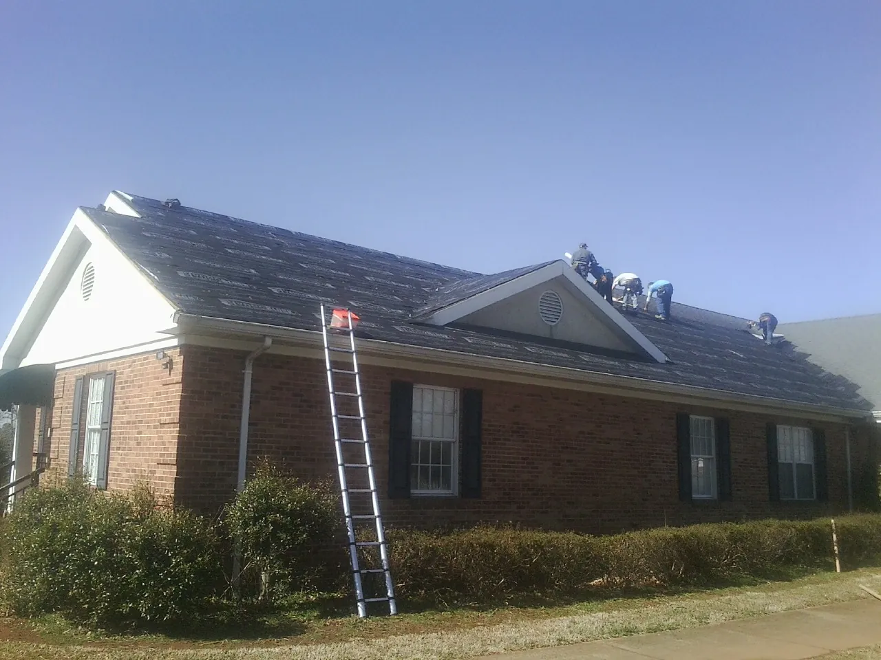 Crew tearing shingles off a brick ranch roof with a ladder set — Emergency Roof Repair work by our crew in Newtown Square