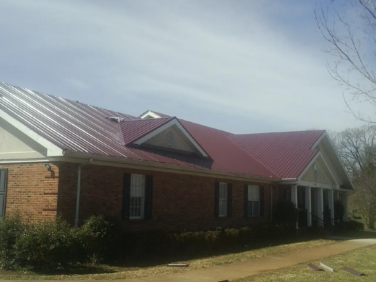 Red metal roof with gabled entries on a long brick building, from a Hail Damage Roof Repair job in Newtown Square