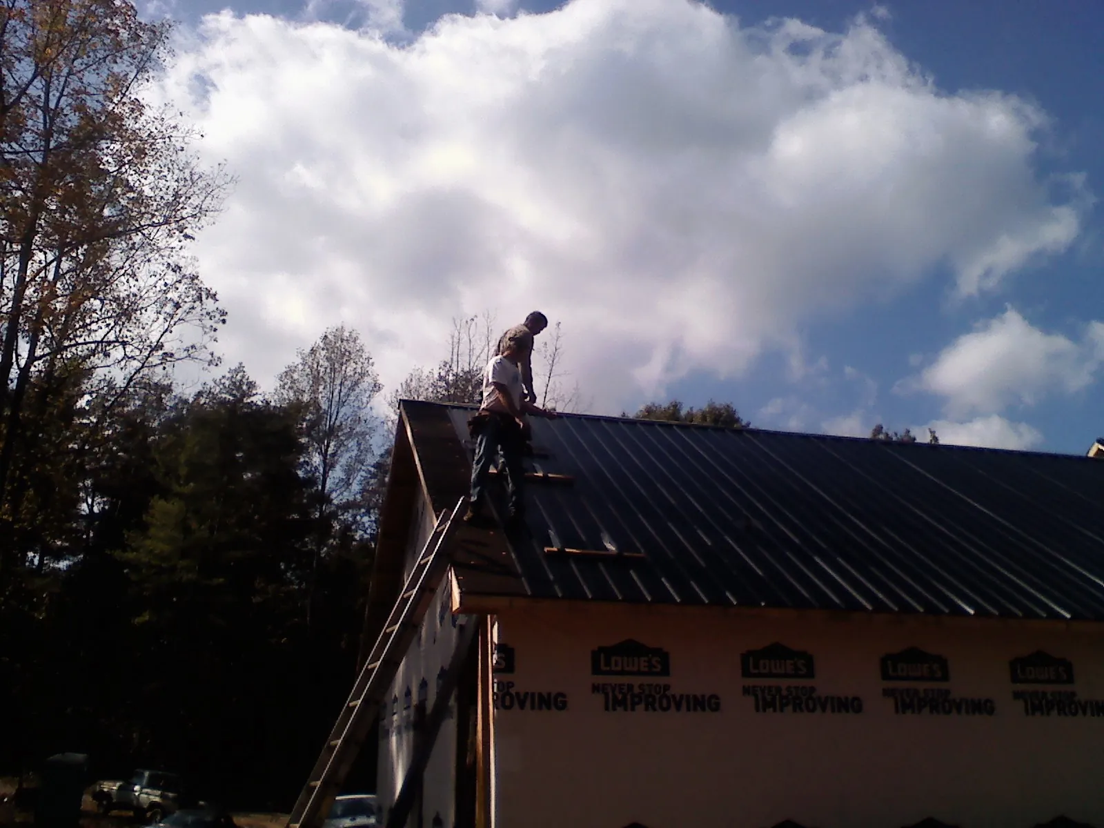 Roofer fastening dark metal panels high against a cloudy sky, from a Roof Inspection job in Newtown Square