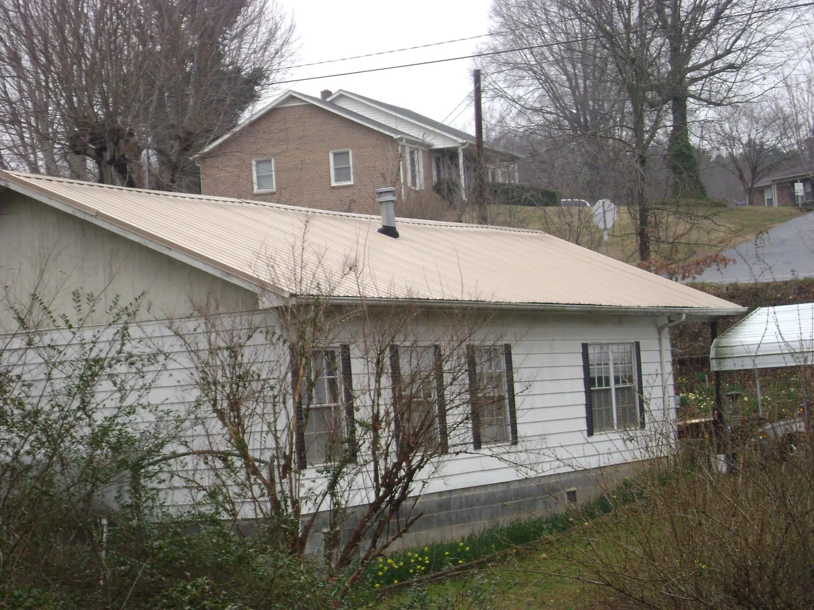 Tan metal roof on a white sided house set into a hillside — Commercial Roofing by Roofing Brothers in Newtown Square